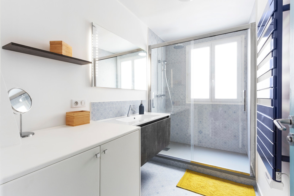 Пример оригинального дизайна: большая ванная комната в современном стиле с монолитной раковиной, плоскими фасадами, белыми фасадами, душем в нише, керамической плиткой, белыми стенами, полом из керамической плитки, душевой кабиной, разноцветной плиткой и окном