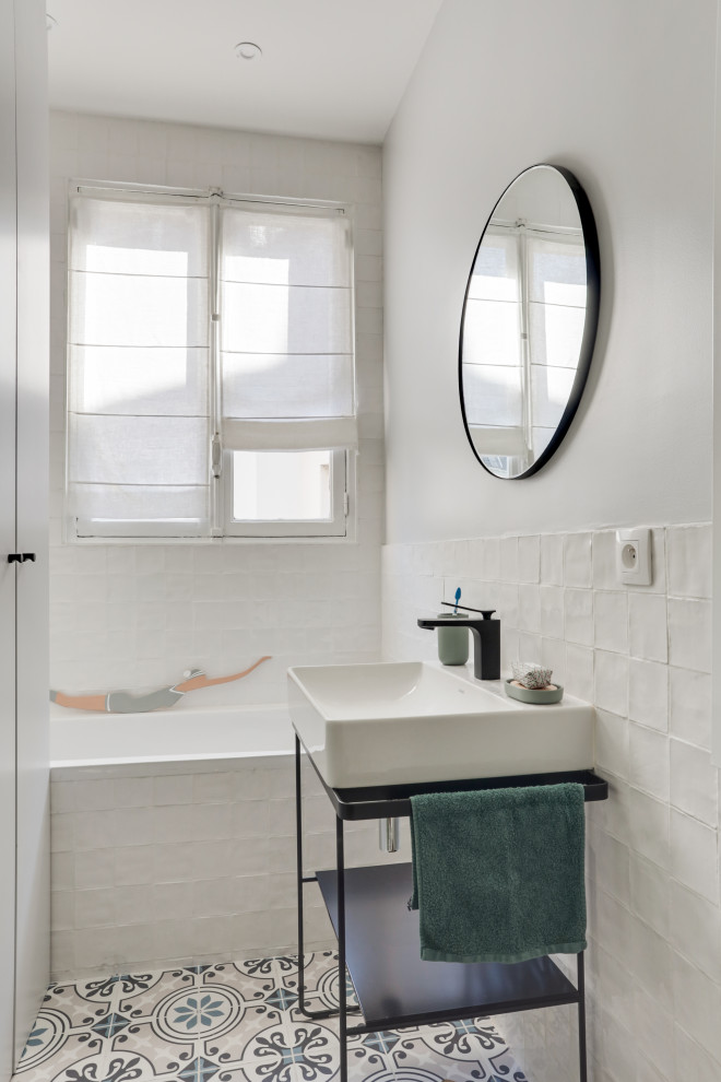 Klassisk inredning av ett litet en-suite badrum, med luckor med profilerade fronter, vita skåp, ett undermonterat badkar, en toalettstol med separat cisternkåpa, vit kakel, perrakottakakel, vita väggar, cementgolv, ett piedestal handfat, blått golv och med dusch som är öppen