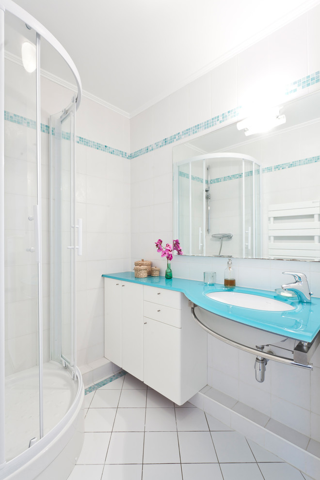 Immagine di una stanza da bagno con doccia design di medie dimensioni con lavabo sottopiano, ante lisce, top in vetro, doccia ad angolo, piastrelle bianche, pareti bianche, pavimento in gres porcellanato, ante bianche e top blu