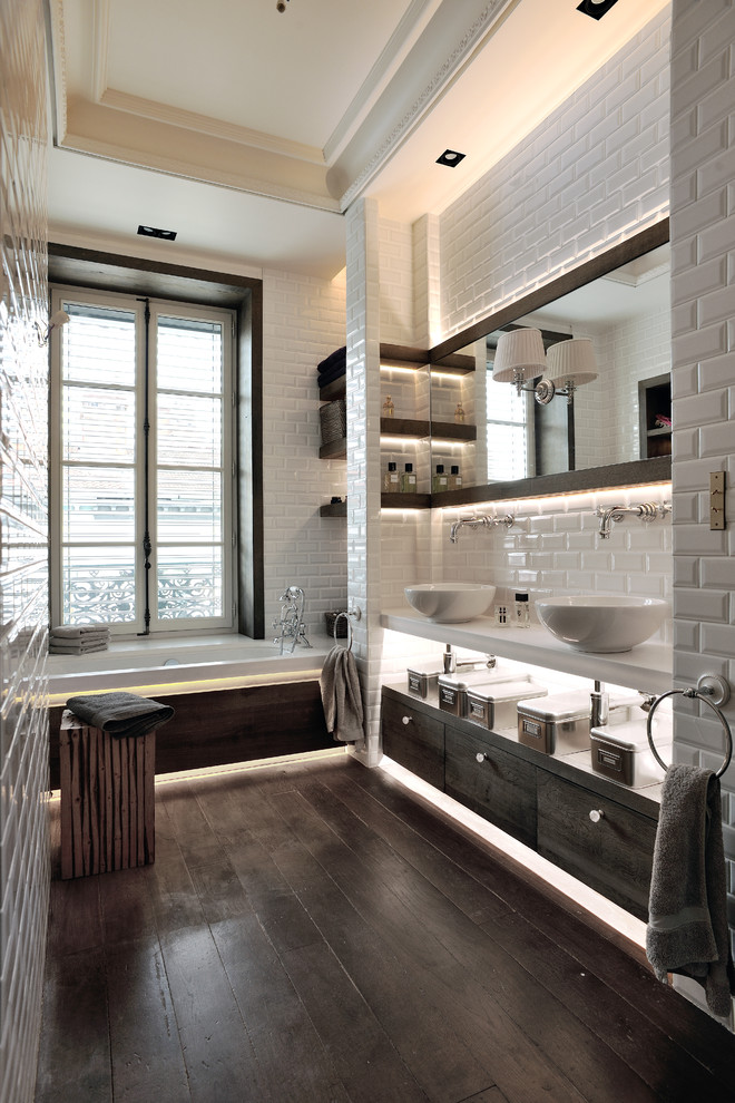 На фото: главная ванная комната в скандинавском стиле с плоскими фасадами, темными деревянными фасадами, ванной в нише, белой плиткой, плиткой кабанчик, белыми стенами, темным паркетным полом, настольной раковиной и коричневым полом