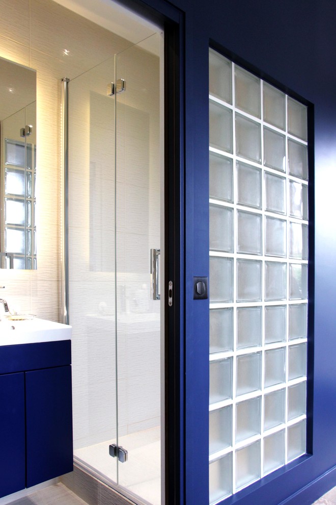 Exemple d'une douche en alcôve tendance avec un placard à porte affleurante, des portes de placard bleues, WC suspendus, un carrelage beige, des carreaux de céramique, un mur beige, un sol en carrelage de céramique et un lavabo encastré.