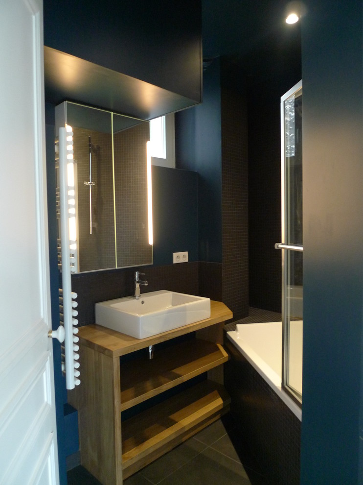 Идея дизайна: маленькая главная ванная комната в современном стиле с светлыми деревянными фасадами, полновстраиваемой ванной, душем над ванной, инсталляцией, черной плиткой, плиткой мозаикой, синими стенами, полом из цементной плитки, накладной раковиной, столешницей из дерева, серым полом, душем с распашными дверями, коричневой столешницей, стеклянными фасадами, тумбой под одну раковину и подвесной тумбой для на участке и в саду
