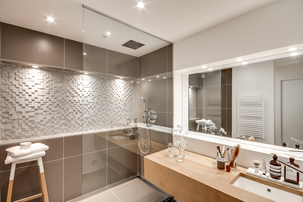 Inredning av ett minimalistiskt mellanstort beige beige badrum med dusch, med brun kakel, en kantlös dusch, ett undermonterad handfat, öppna hyllor, skåp i mellenmörkt trä, en vägghängd toalettstol, keramikplattor, vita väggar, klinkergolv i keramik, träbänkskiva, grått golv och dusch med gångjärnsdörr
