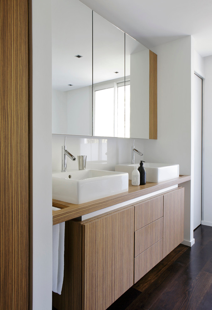 Ejemplo de cuarto de baño actual de tamaño medio con lavabo sobreencimera, armarios con paneles lisos, puertas de armario de madera oscura, paredes blancas y suelo de madera oscura