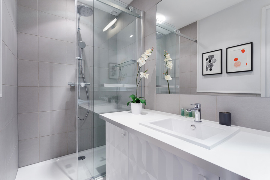 Modern inredning av ett litet vit vitt en-suite badrum, med luckor med profilerade fronter, vita skåp, en kantlös dusch, en vägghängd toalettstol, grå kakel, keramikplattor, grå väggar, klinkergolv i keramik, ett undermonterad handfat, bänkskiva i akrylsten, grått golv och dusch med skjutdörr