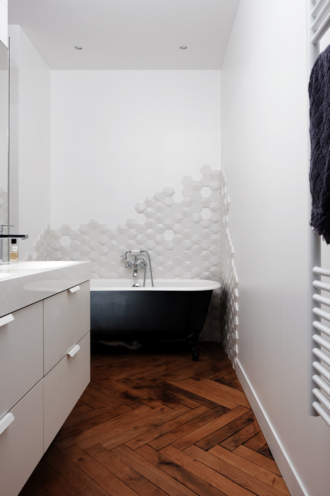 Modelo de cuarto de baño contemporáneo con armarios con paneles lisos, puertas de armario grises, bañera con patas, baldosas y/o azulejos grises, paredes blancas, suelo de madera oscura, aseo y ducha, lavabo integrado, suelo marrón y encimeras blancas