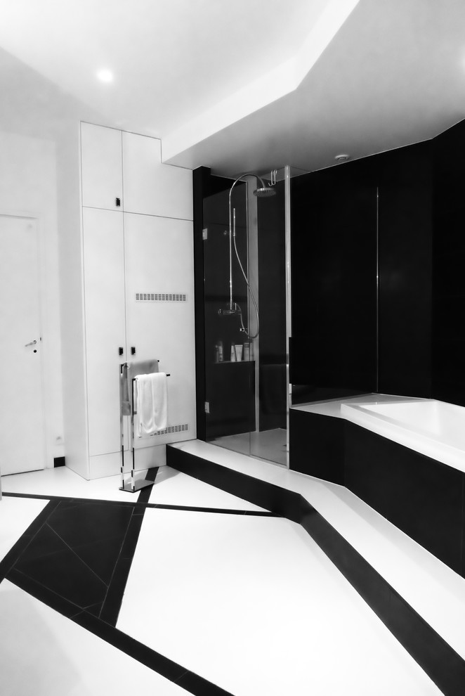 Modernes Badezimmer mit Kassettenfronten, schwarzen Schränken, Eckbadewanne, Nasszelle, schwarz-weißen Fliesen, schwarzer Wandfarbe, Laminat, Mineralwerkstoff-Waschtisch, schwarzem Boden und Falttür-Duschabtrennung in Paris