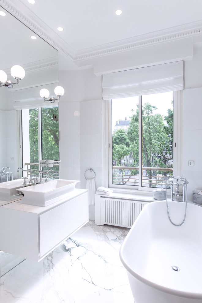 Cette photo montre une salle de bain chic de taille moyenne avec des portes de placard blanches, une baignoire indépendante, un mur blanc, un sol en marbre, une vasque et une fenêtre.