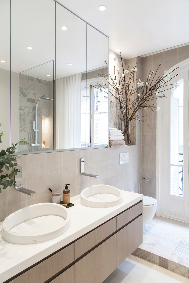 Aménagement d'une salle de bain scandinave en bois clair avec un placard à porte plane, WC suspendus, un carrelage beige, un mur beige, une vasque et un plan de toilette blanc.