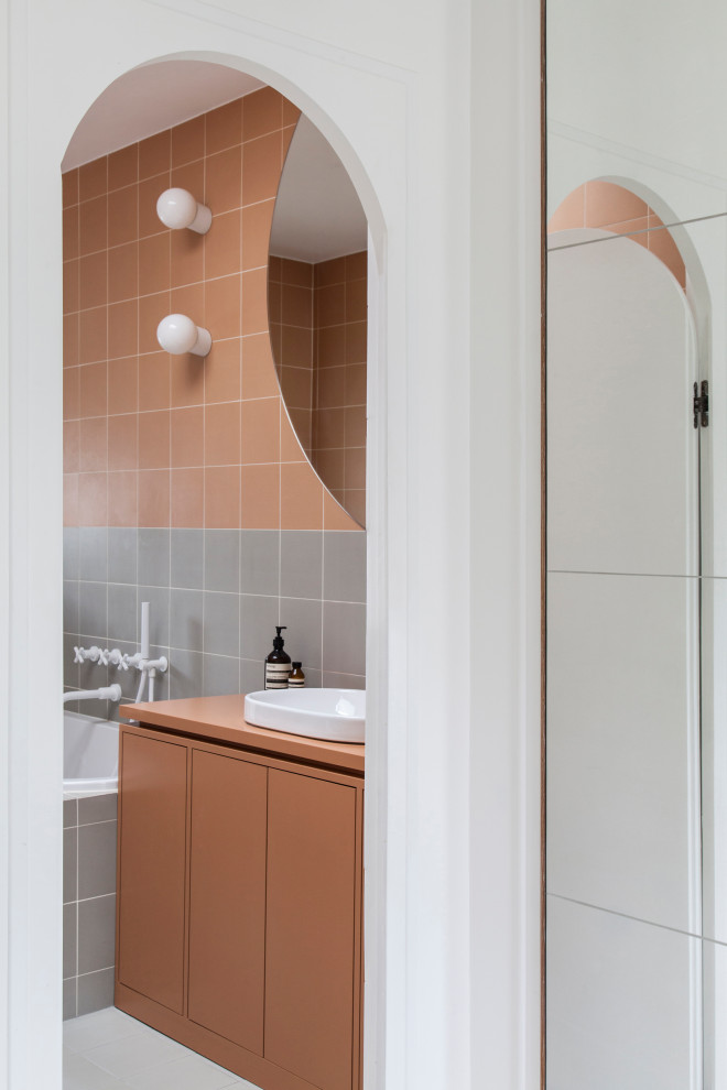 Cette image montre une salle de bain design avec un placard à porte plane, des portes de placard oranges, un carrelage gris, un carrelage orange, une vasque, un sol blanc, un plan de toilette orange et meuble simple vasque.