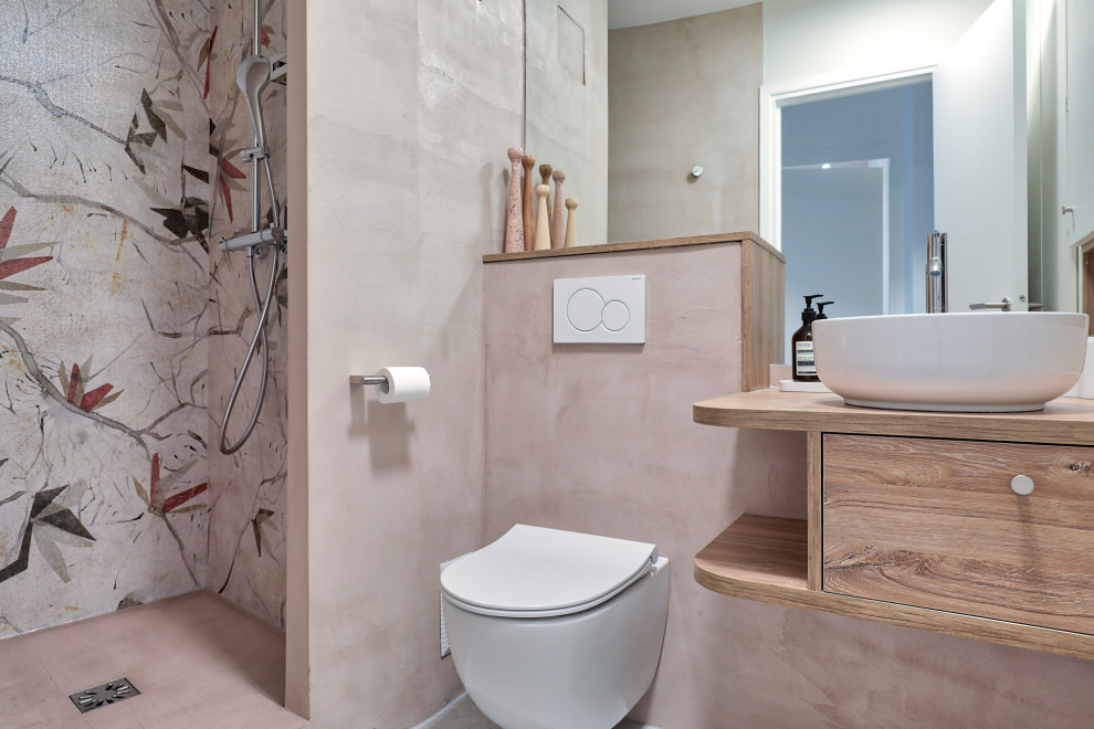 Стильный дизайн: ванная комната среднего размера в стиле модернизм с фасадами с декоративным кантом, светлыми деревянными фасадами, открытым душем, инсталляцией, розовой плиткой, розовыми стенами, полом из терраццо, душевой кабиной, накладной раковиной, столешницей из дерева, серым полом, открытым душем, коричневой столешницей, тумбой под одну раковину, подвесной тумбой и обоями на стенах - последний тренд