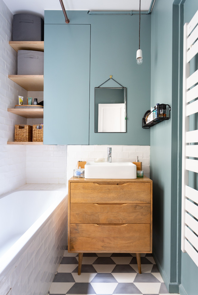 Exempel på ett litet minimalistiskt brun brunt en-suite badrum, med skåp i mellenmörkt trä, ett platsbyggt badkar, vit kakel, blå väggar, ett fristående handfat, träbänkskiva, flerfärgat golv, släta luckor, en dusch/badkar-kombination, en vägghängd toalettstol, tunnelbanekakel, cementgolv och med dusch som är öppen