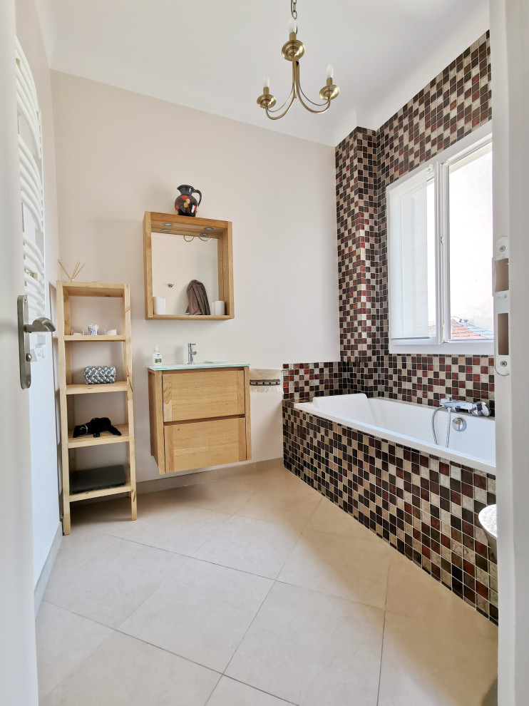 На фото: маленькая главная ванная комната в стиле модернизм с плоскими фасадами, светлыми деревянными фасадами, ванной в нише, душевой комнатой, разноцветной плиткой, плиткой мозаикой, бежевыми стенами, полом из керамической плитки, настольной раковиной, стеклянной столешницей, бежевым полом, открытым душем и бирюзовой столешницей для на участке и в саду