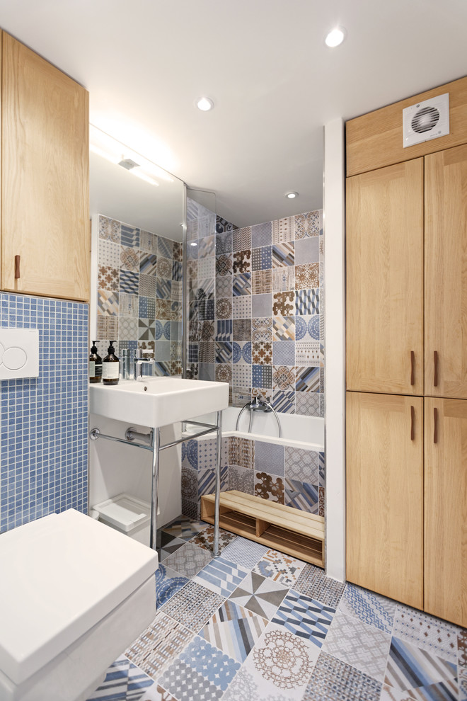 Modern inredning av ett mellanstort en-suite badrum, med skåp i ljust trä, ett badkar i en alkov, en dusch/badkar-kombination, en vägghängd toalettstol, beige kakel, vit kakel, blå kakel, cementkakel, vita väggar, klinkergolv i keramik och ett konsol handfat