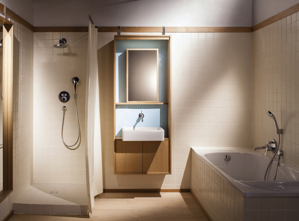 Cette image montre une grande salle de bain principale design en bois clair avec un placard sans porte, une baignoire d'angle, une douche ouverte, un carrelage beige, un mur beige, parquet clair et un lavabo suspendu.