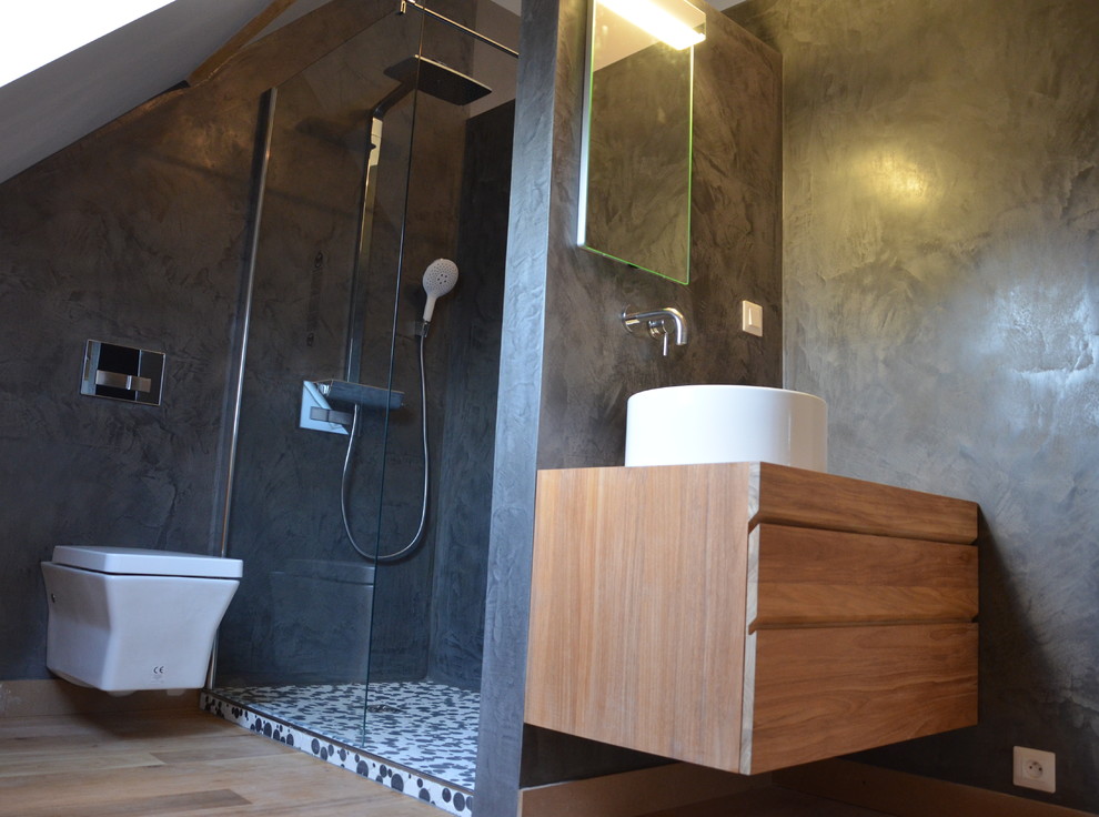 Diseño de cuarto de baño contemporáneo con lavabo suspendido, ducha esquinera, baldosas y/o azulejos negros, baldosas y/o azulejos en mosaico, paredes grises, suelo de madera clara y aseo y ducha