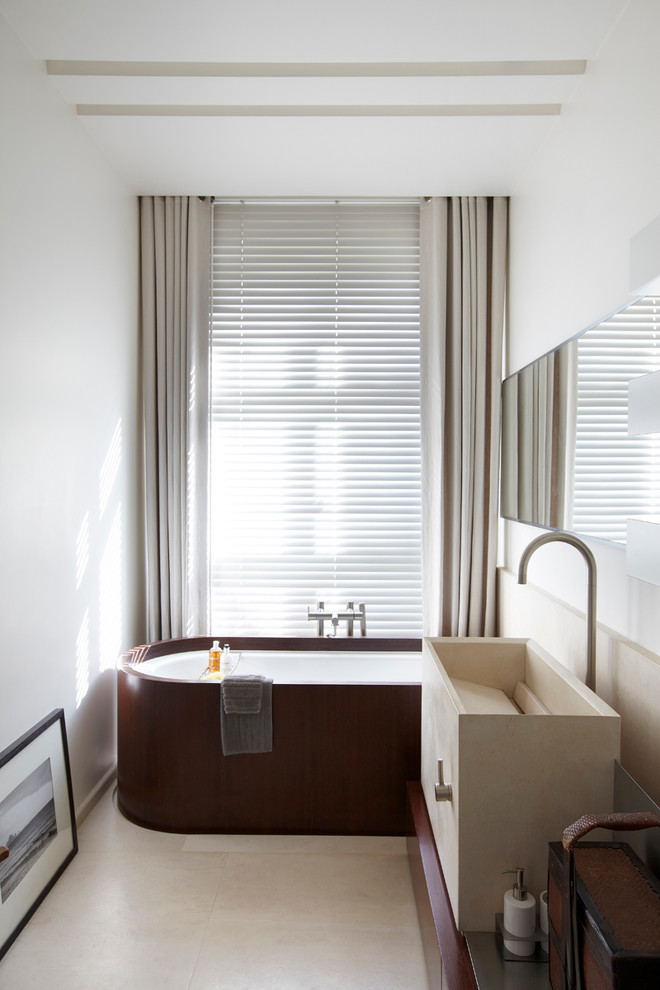 Ejemplo de cuarto de baño principal actual de tamaño medio con bañera exenta, paredes blancas, suelo de baldosas de cerámica, lavabo integrado y encimera de madera