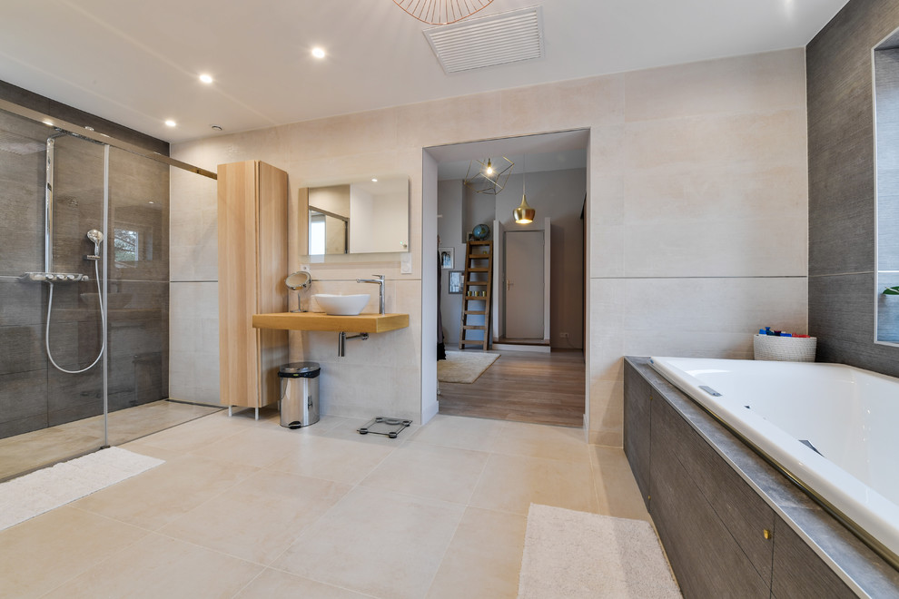 Idéer för mellanstora funkis beige en-suite badrum, med en jacuzzi, en kantlös dusch, grå kakel, keramikplattor, beige väggar, klinkergolv i keramik, ett fristående handfat, träbänkskiva, beiget golv och dusch med skjutdörr