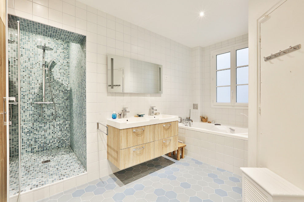 Cette image montre une grande salle de bain principale traditionnelle en bois clair avec une douche à l'italienne, un carrelage blanc, un mur blanc, un sol en carrelage de céramique, un sol bleu, une cabine de douche à porte battante, des carreaux de céramique, un placard à porte affleurante, un bain bouillonnant, WC suspendus, un lavabo intégré, un plan de toilette en surface solide, un plan de toilette blanc, meuble double vasque, meuble-lavabo suspendu et du carrelage bicolore.