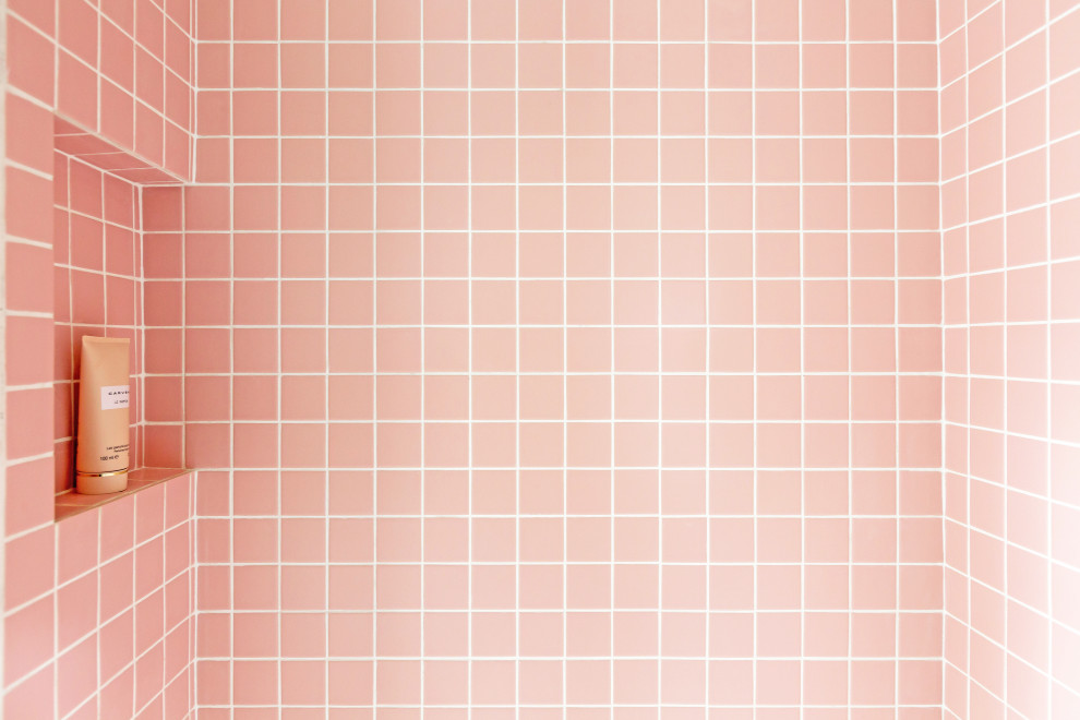 Modelo de cuarto de baño romántico pequeño con armarios con rebordes decorativos, puertas de armario blancas, ducha esquinera, sanitario de pared, baldosas y/o azulejos rosa, baldosas y/o azulejos de cerámica, paredes blancas, suelo de terrazo, aseo y ducha, lavabo tipo consola, encimera de terrazo, suelo multicolor, ducha con puerta con bisagras y encimeras rosas