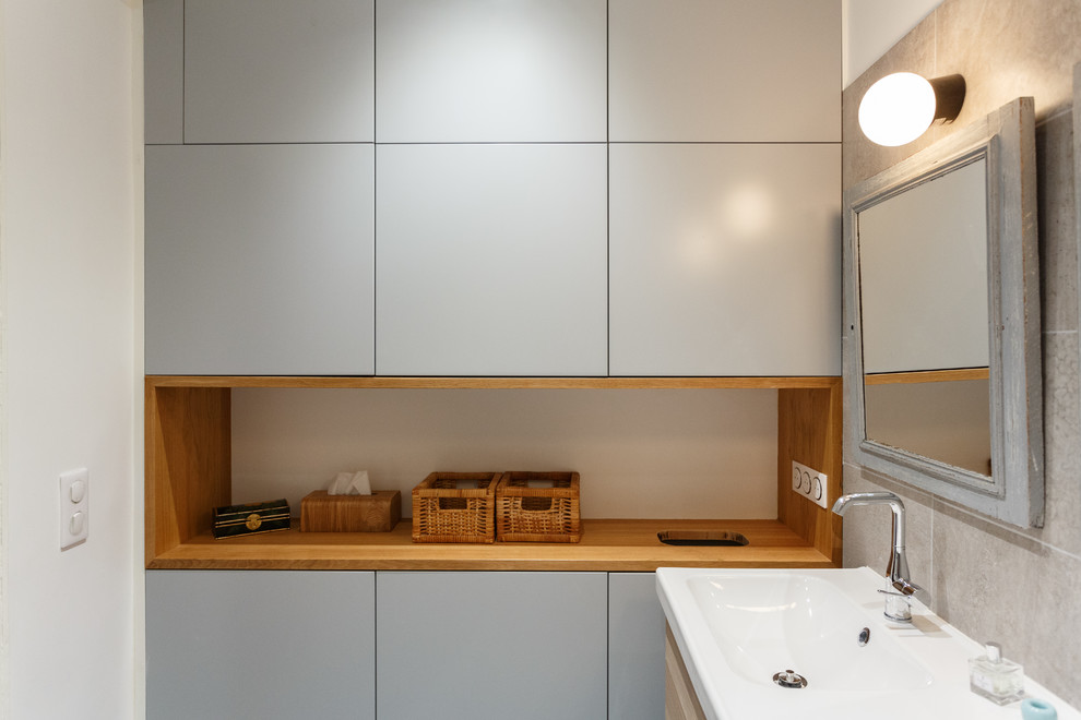 Photo of a small contemporary ensuite bathroom in Paris with flat-panel cabinets, light wood cabinets, a submerged bath, beige tiles, ceramic tiles, ceramic flooring, a trough sink, solid surface worktops, grey floors and white worktops.