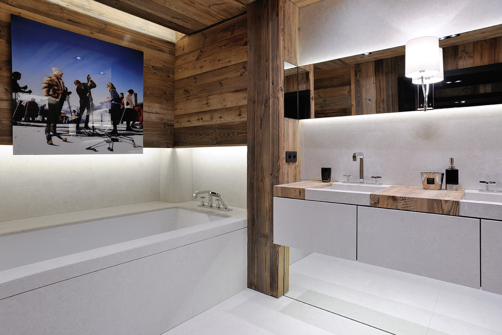 Aménagement d'une salle de bain principale montagne avec un placard à porte plane, des portes de placard grises, une baignoire encastrée et un plan de toilette en bois.