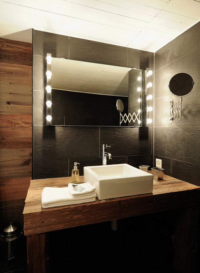 Diseño de cuarto de baño principal rústico con lavabo sobreencimera, armarios abiertos, puertas de armario con efecto envejecido, encimera de madera, baldosas y/o azulejos negros, baldosas y/o azulejos de piedra, paredes negras y suelo de pizarra