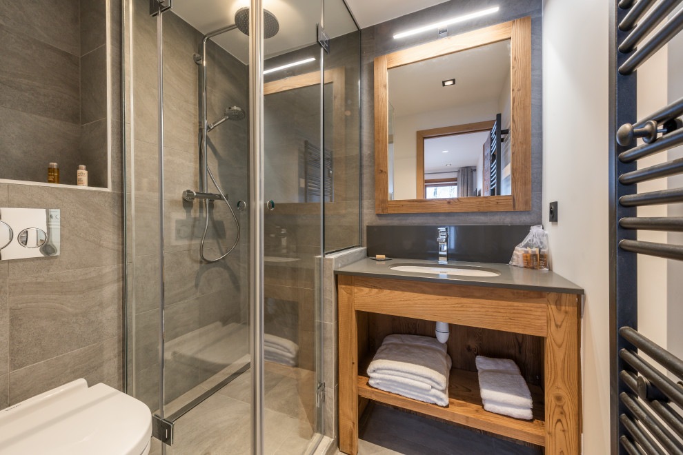 Medium sized rustic shower room bathroom in Grenoble with open cabinets, medium wood cabinets, a corner shower, a wall mounted toilet, grey tiles, white walls, a submerged sink, grey floors, a hinged door, grey worktops, a single sink and a built in vanity unit.