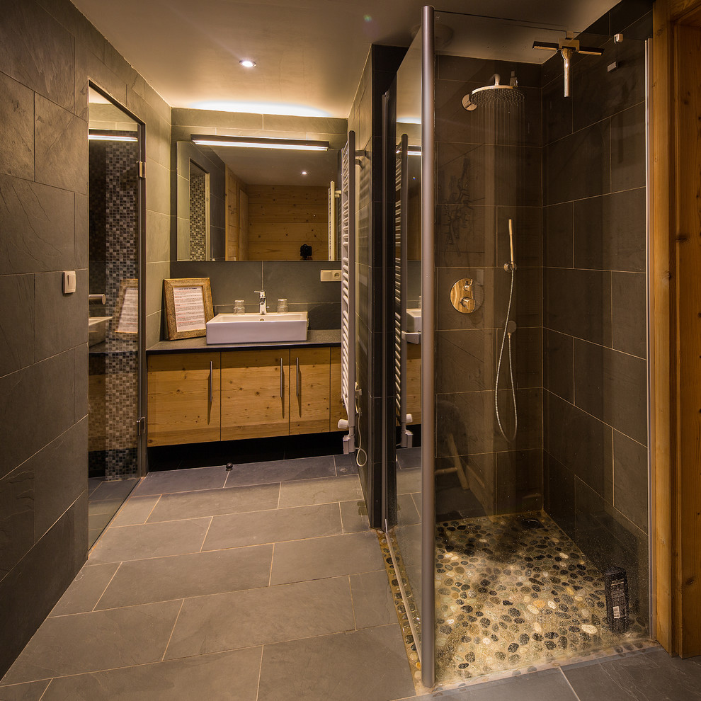 Foto på ett stort rustikt en-suite badrum, med luckor med upphöjd panel, skåp i slitet trä, en kantlös dusch, svart kakel, skifferkakel, svarta väggar, skiffergolv och ett nedsänkt handfat