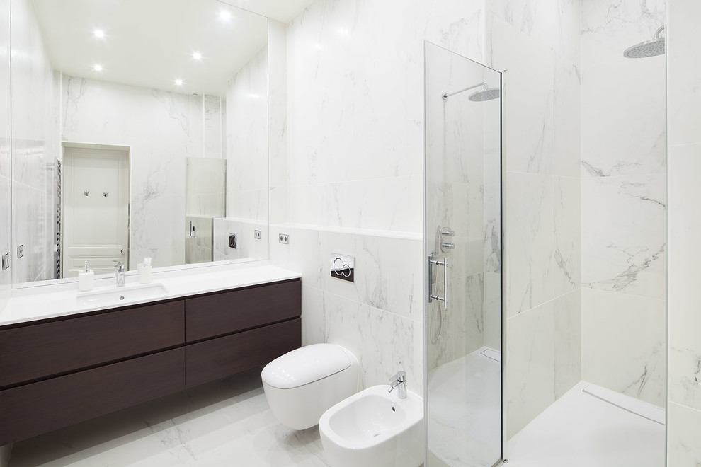 Cette image montre une grande salle de bain principale design en bois foncé avec WC suspendus, un carrelage blanc, des carreaux de céramique, un mur blanc, un sol en carrelage de céramique, un lavabo encastré et un plan de toilette en quartz.
