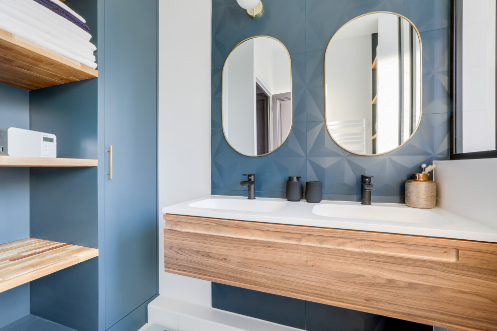 This is an example of a contemporary bathroom in Paris with flat-panel cabinets, medium wood cabinets, blue tiles, white walls, an integrated sink, white worktops, double sinks and a floating vanity unit.