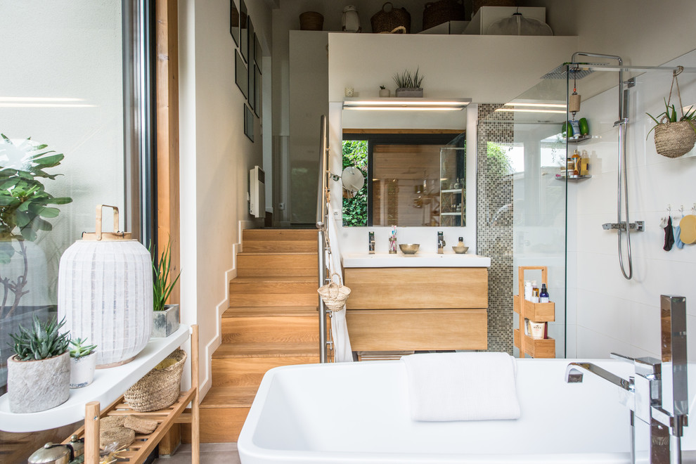 Duschbad mit flächenbündigen Schrankfronten, hellbraunen Holzschränken, freistehender Badewanne, Eckdusche, weißen Fliesen, weißer Wandfarbe und Waschtischkonsole in Paris