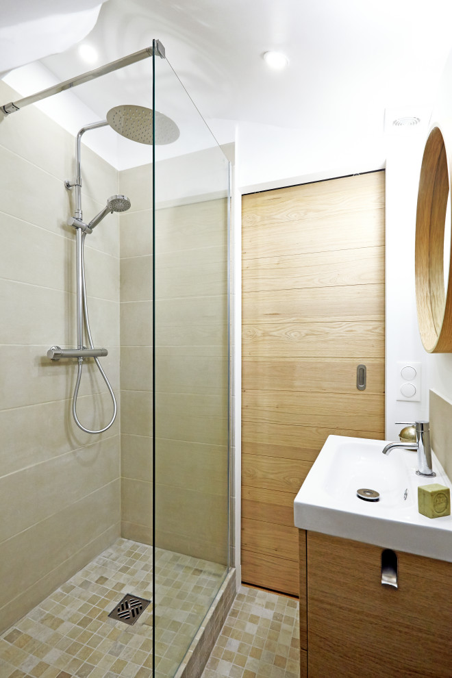 Foto på ett litet funkis beige badrum med dusch, med släta luckor, beige skåp, en kantlös dusch, en vägghängd toalettstol, beige kakel, keramikplattor, vita väggar, mosaikgolv, ett avlångt handfat, träbänkskiva, beiget golv och med dusch som är öppen