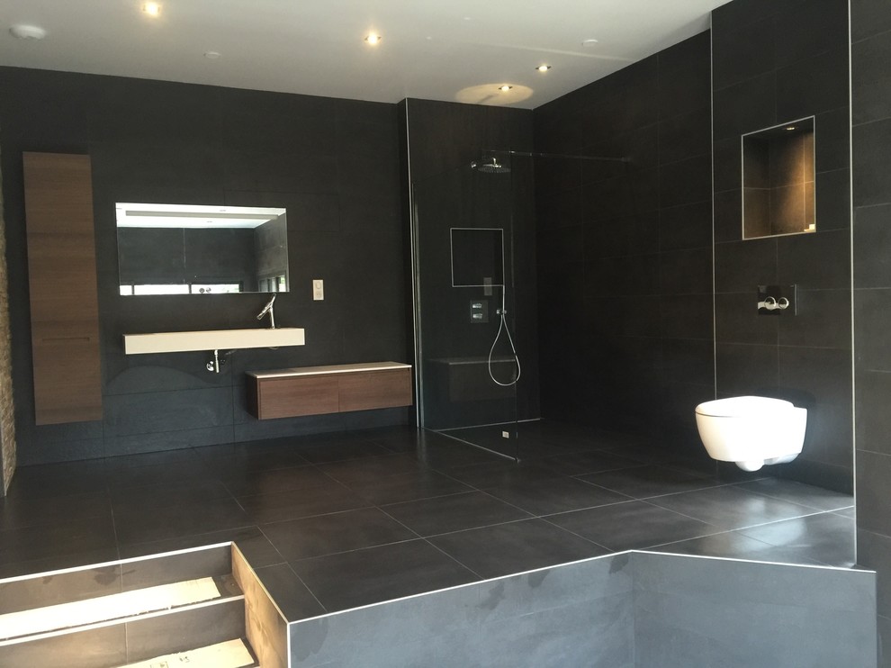 Inspiration för ett mycket stort funkis en-suite badrum, med skåp i mellenmörkt trä, en kantlös dusch, en vägghängd toalettstol, svart kakel, stenkakel, svarta väggar, skiffergolv och ett fristående handfat