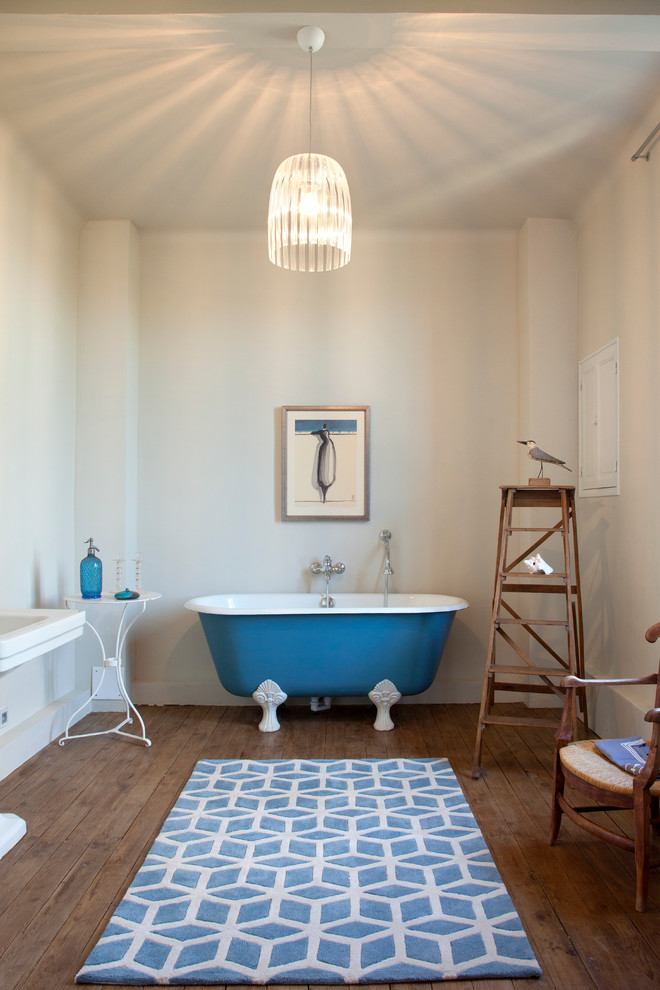 Réalisation d'une salle de bain principale marine avec une baignoire indépendante, un mur beige, un sol en bois brun et un sol bleu.