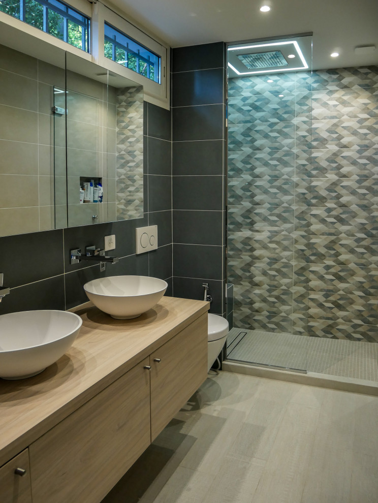 Photo of a contemporary ensuite bathroom in Nice with grey tiles, grey walls, a wall-mounted sink, beige floors, beige worktops, flat-panel cabinets, beige cabinets, an alcove shower, a wall mounted toilet, porcelain tiles and wooden worktops.