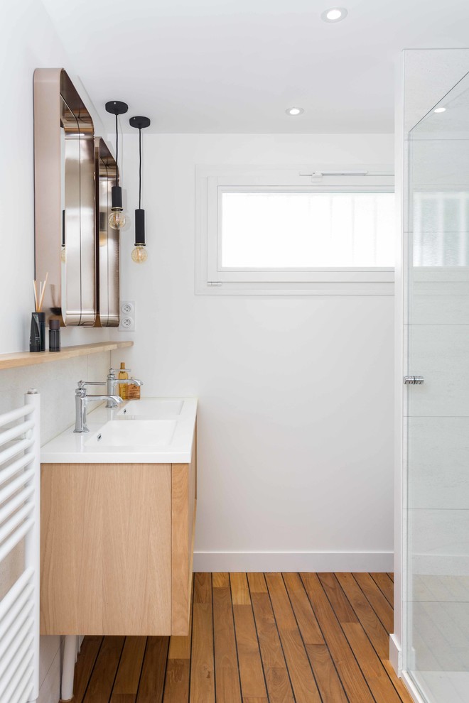 Idées déco pour une salle de bain contemporaine en bois clair avec un placard à porte plane, un carrelage blanc, un mur blanc, un sol en bois brun, un plan vasque, un sol marron, une cabine de douche à porte battante et un plan de toilette blanc.