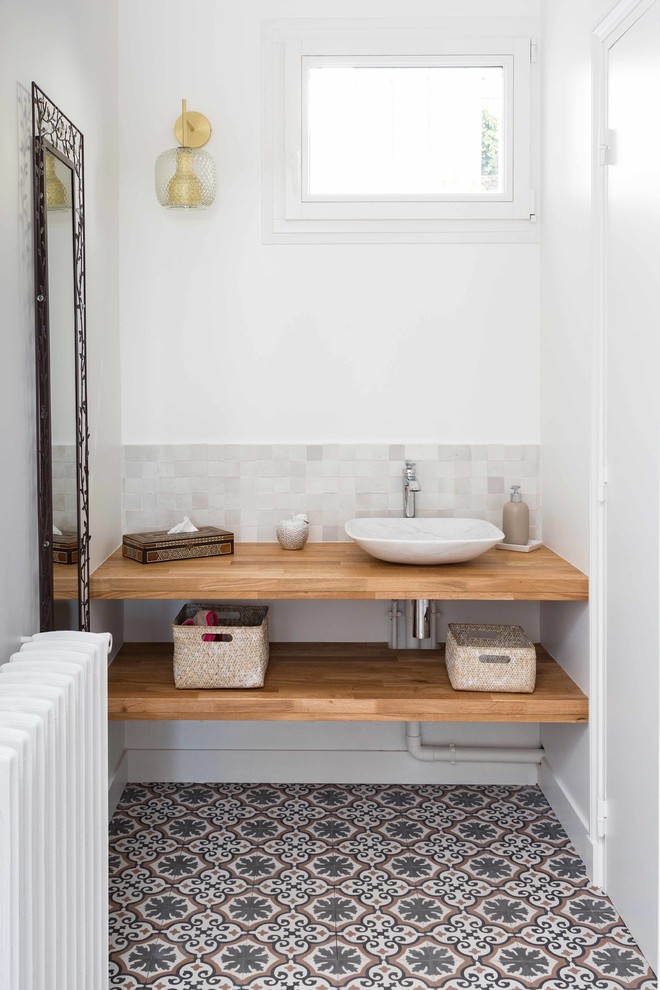 Cette image montre une salle de bain design avec un mur blanc, une vasque, un plan de toilette en bois, un sol multicolore, un plan de toilette beige et un placard sans porte.