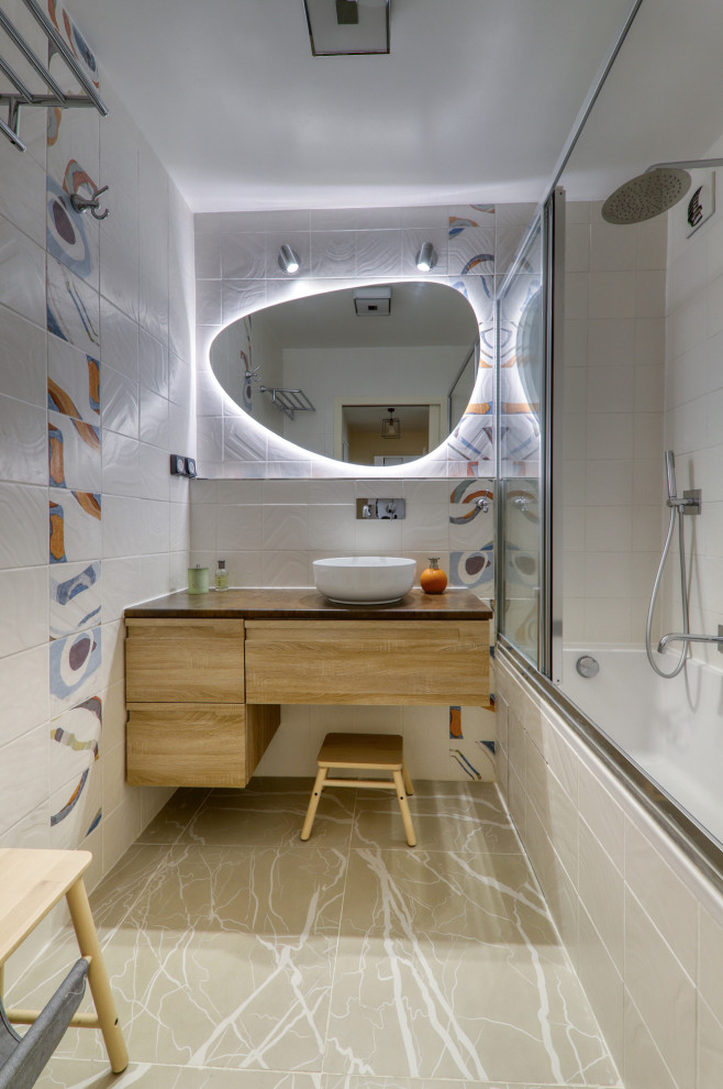 На фото: детская ванная комната среднего размера в современном стиле с ванной в нише, душем над ванной, разноцветной плиткой, бежевой плиткой, бежевым полом, плоскими фасадами, светлыми деревянными фасадами, керамогранитной плиткой, полом из керамогранита, настольной раковиной, душем с раздвижными дверями, коричневой столешницей и подвесной тумбой с
