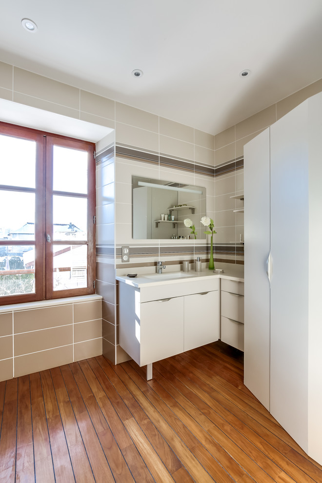 Inspiration pour une grande salle de bain design avec un placard à porte affleurante, des portes de placard beiges, WC suspendus, un mur beige, un sol en bois brun, un plan vasque et un plan de toilette en surface solide.