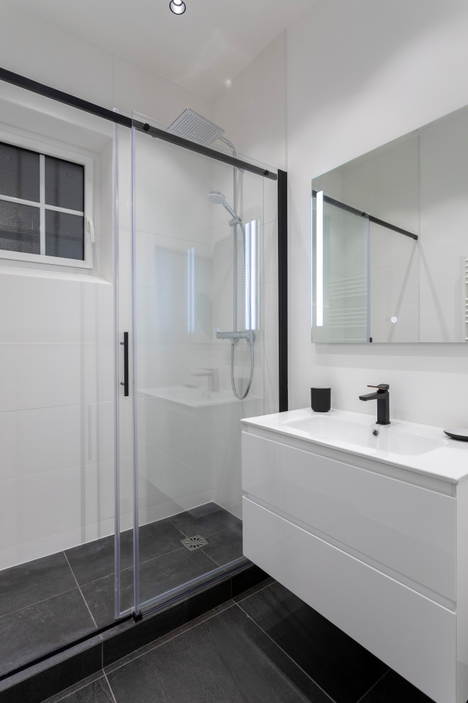 Inredning av ett modernt litet vit vitt badrum med dusch, med luckor med profilerade fronter, vita skåp, en kantlös dusch, vit kakel, keramikplattor, vita väggar, klinkergolv i keramik, ett konsol handfat, bänkskiva i täljsten, svart golv och dusch med skjutdörr