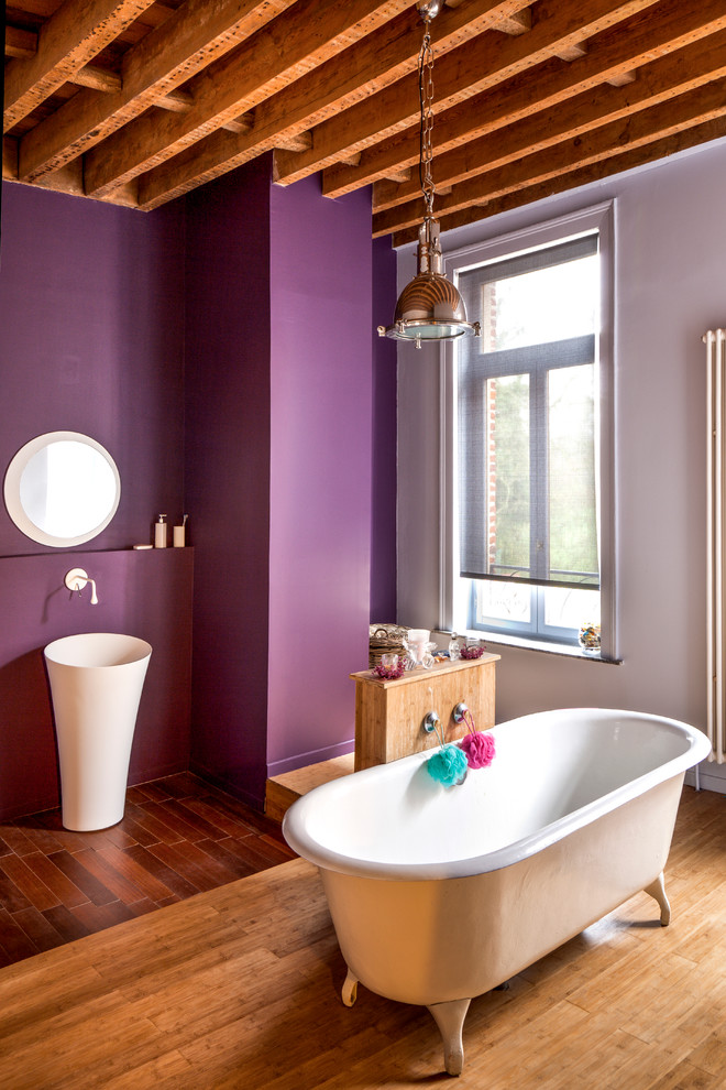 Réalisation d'une salle de bain principale design de taille moyenne avec un lavabo suspendu, une baignoire sur pieds, un mur violet et un sol en bois brun.