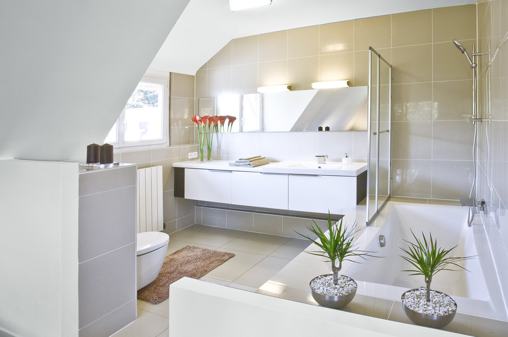 Inspiration för ett mellanstort funkis en-suite badrum, med släta luckor, vita skåp, ett platsbyggt badkar, en dusch/badkar-kombination, beige kakel, keramikplattor, beige väggar, en vägghängd toalettstol och ett integrerad handfat