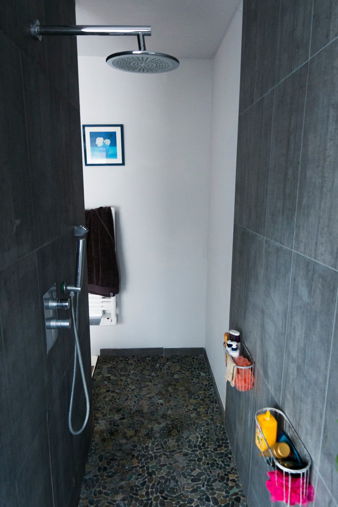 Modelo de cuarto de baño actual de tamaño medio con ducha abierta, baldosas y/o azulejos grises, baldosas y/o azulejos de cerámica, paredes blancas, suelo de baldosas tipo guijarro, aseo y ducha, lavabo integrado, suelo gris y ducha abierta