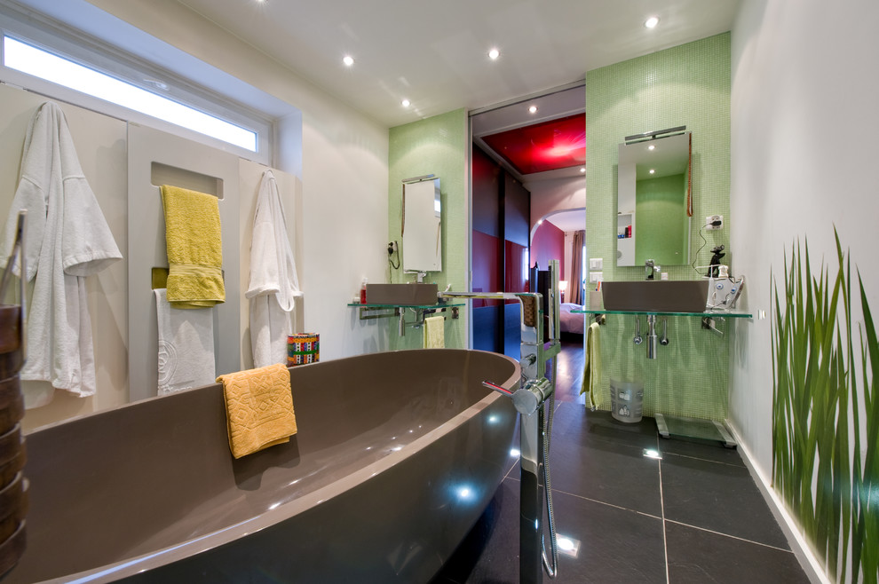 Cette photo montre une salle de bain principale tendance de taille moyenne avec une grande vasque, un plan de toilette en verre, une baignoire indépendante, une douche à l'italienne, WC suspendus, un carrelage vert, mosaïque et un mur blanc.