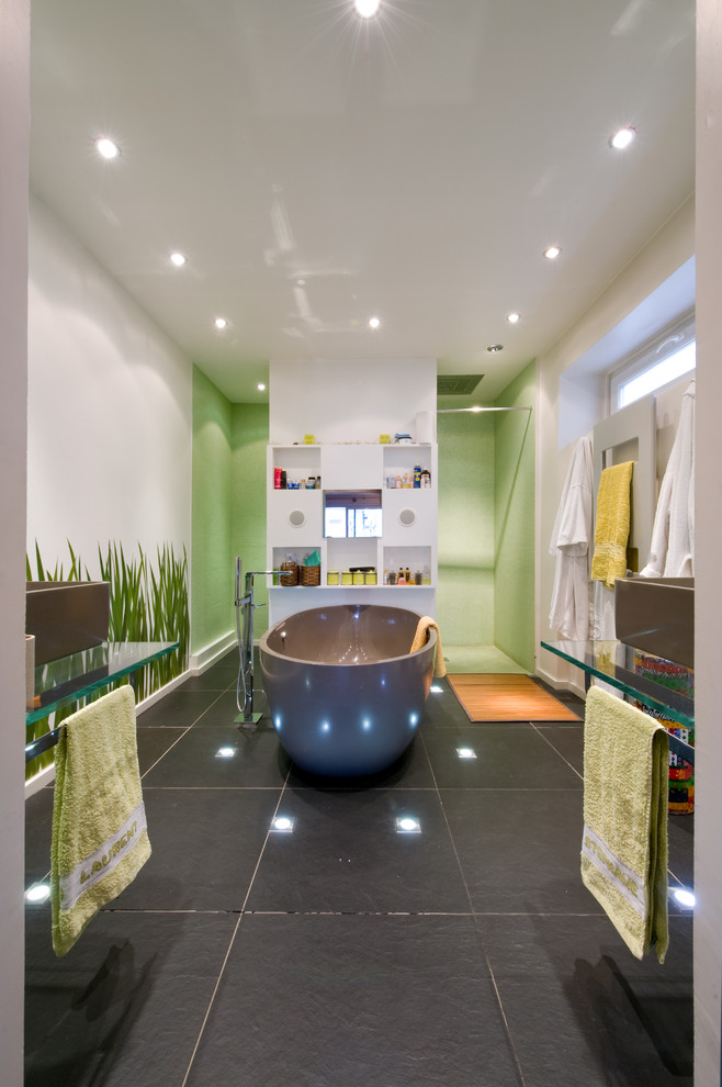 Inredning av ett modernt mellanstort en-suite badrum, med ett avlångt handfat, bänkskiva i glas, ett fristående badkar, en kantlös dusch, en vägghängd toalettstol, grön kakel, mosaik och vita väggar