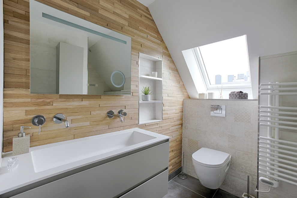 Bild på ett skandinaviskt vit vitt badrum, med släta luckor, vita skåp, en vägghängd toalettstol, beige väggar, ett avlångt handfat och grått golv