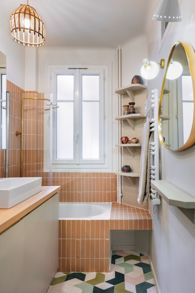 Bild på ett litet funkis en-suite badrum, med keramikplattor, cementgolv, träbänkskiva, vita skåp, ett hörnbadkar, en dusch/badkar-kombination, rosa kakel, rosa väggar, ett nedsänkt handfat, flerfärgat golv och dusch med gångjärnsdörr