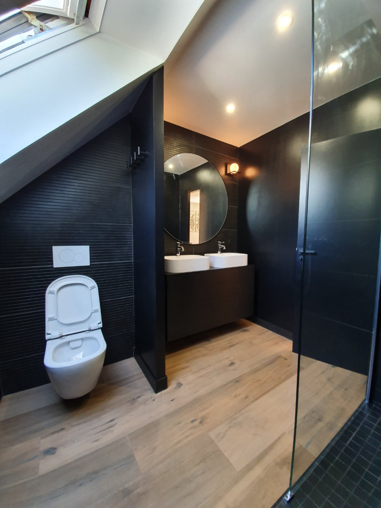 Inredning av ett modernt mellanstort svart svart en-suite badrum, med en kantlös dusch, en vägghängd toalettstol, svart kakel, porslinskakel, svarta väggar, ett väggmonterat handfat, träbänkskiva, beiget golv och med dusch som är öppen