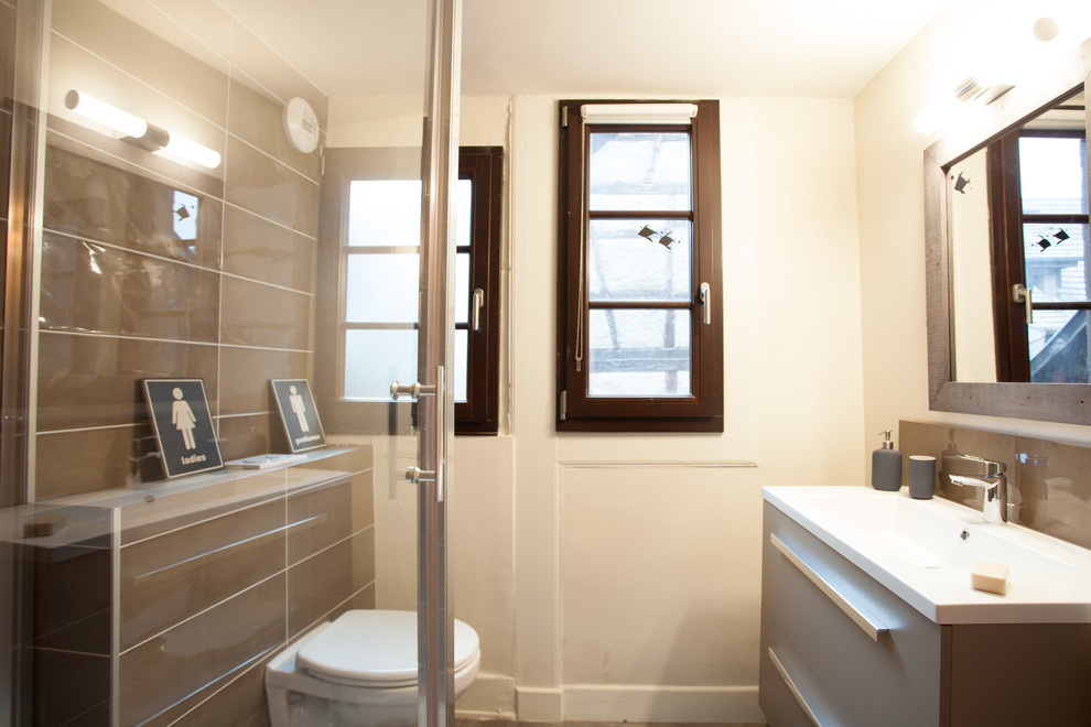 Example of a small urban 3/4 brown tile and porcelain tile slate floor and black floor walk-in shower design in Strasbourg with open cabinets, brown cabinets, a wall-mount toilet, beige walls, a console sink, solid surface countertops and a hinged shower door